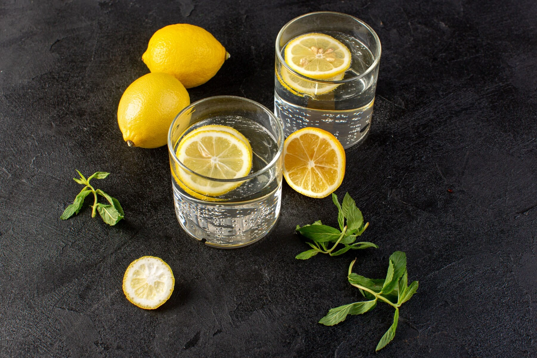 a-front-view-water-with-lemon-fresh-cool-drink-with-sliced-lemons-along-with-whole-lemons-and-leaves-inside-transparent-glasses-on-the-dark_140725-18360.jpg