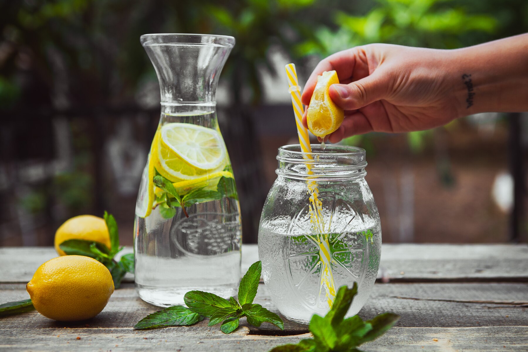 hand-squeezing-lemon-into-a-glass-jar-with-water-side-view-on-wooden-and-yard-table_176474-5965.jpg